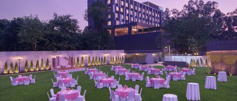 A formal outdoor event space with multiple round tables set up on a green lawn, surrounded by white chairs.