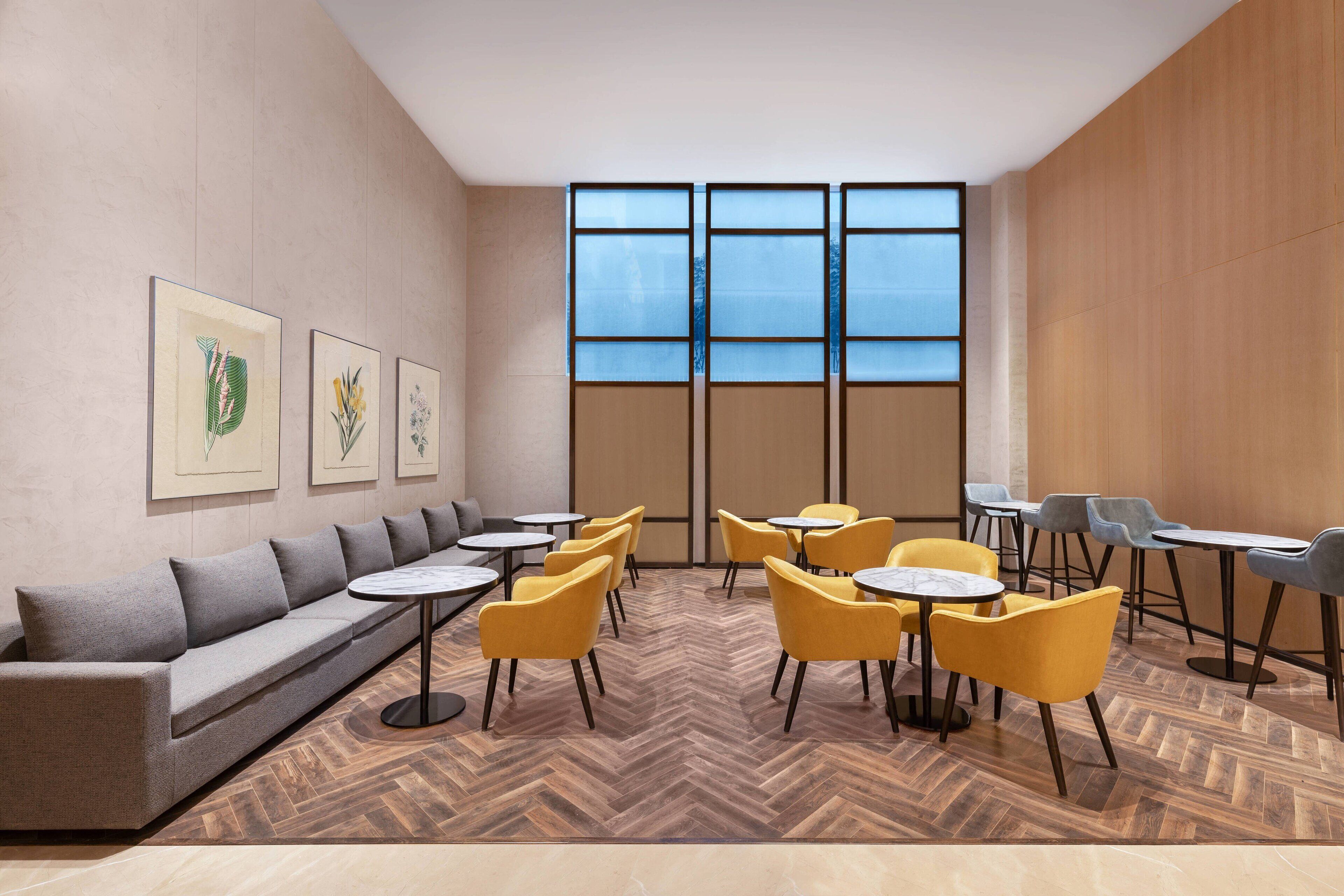 Un salón moderno con un sofá, sillones amarillos y mesas dispuestas en un patrón en forma de chevron.