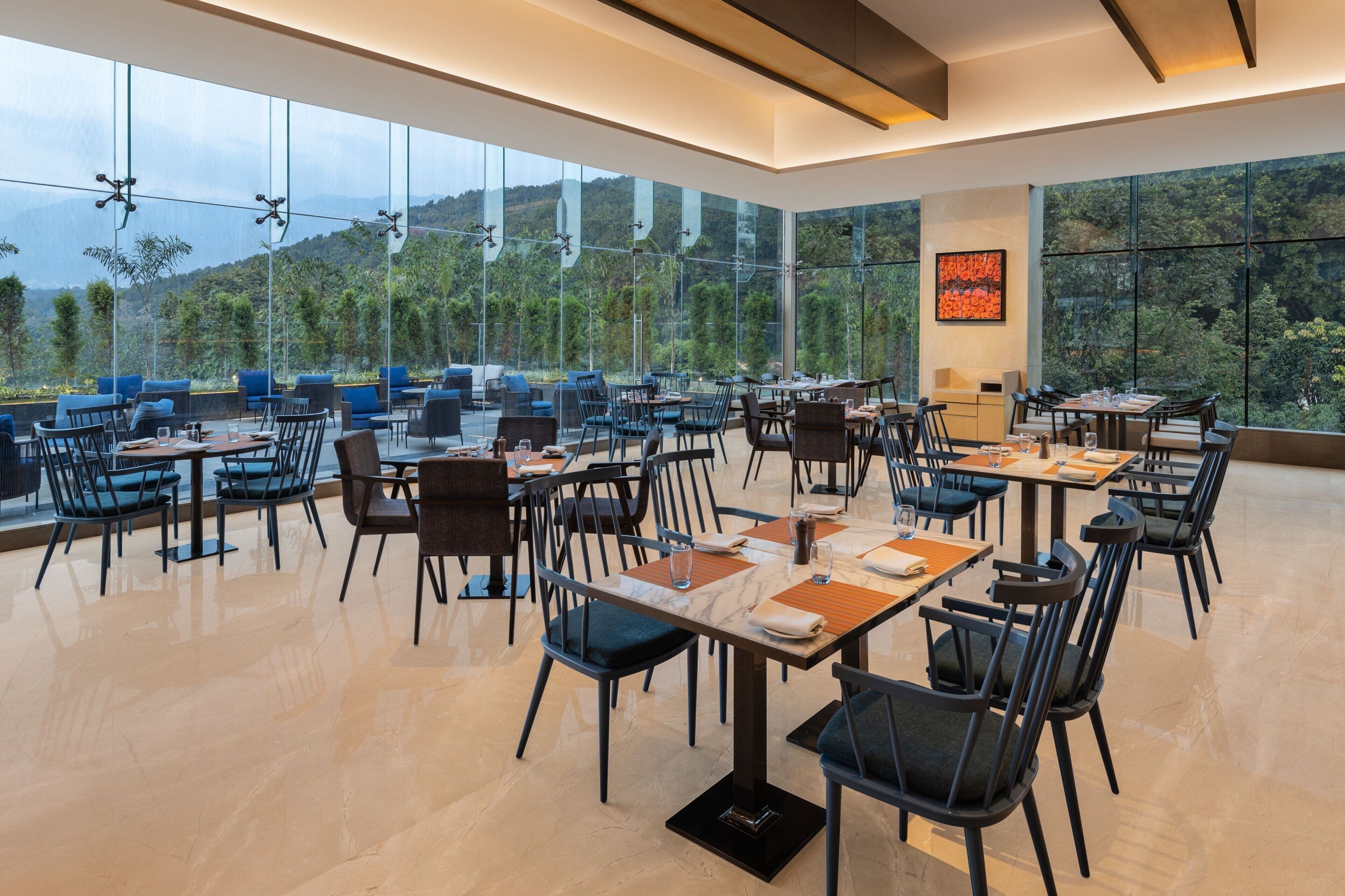 A spacious dining area with tables and chairs arranged for guests, large windows offering a view of the outdoors, and a modern interior design.