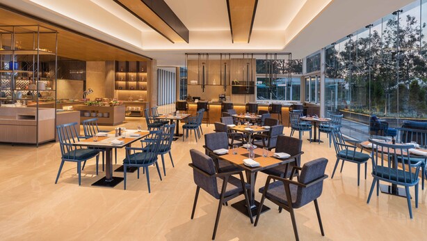 Un comedor moderno con mesas y sillas, una zona de cocina y grandes ventanales con vistas.