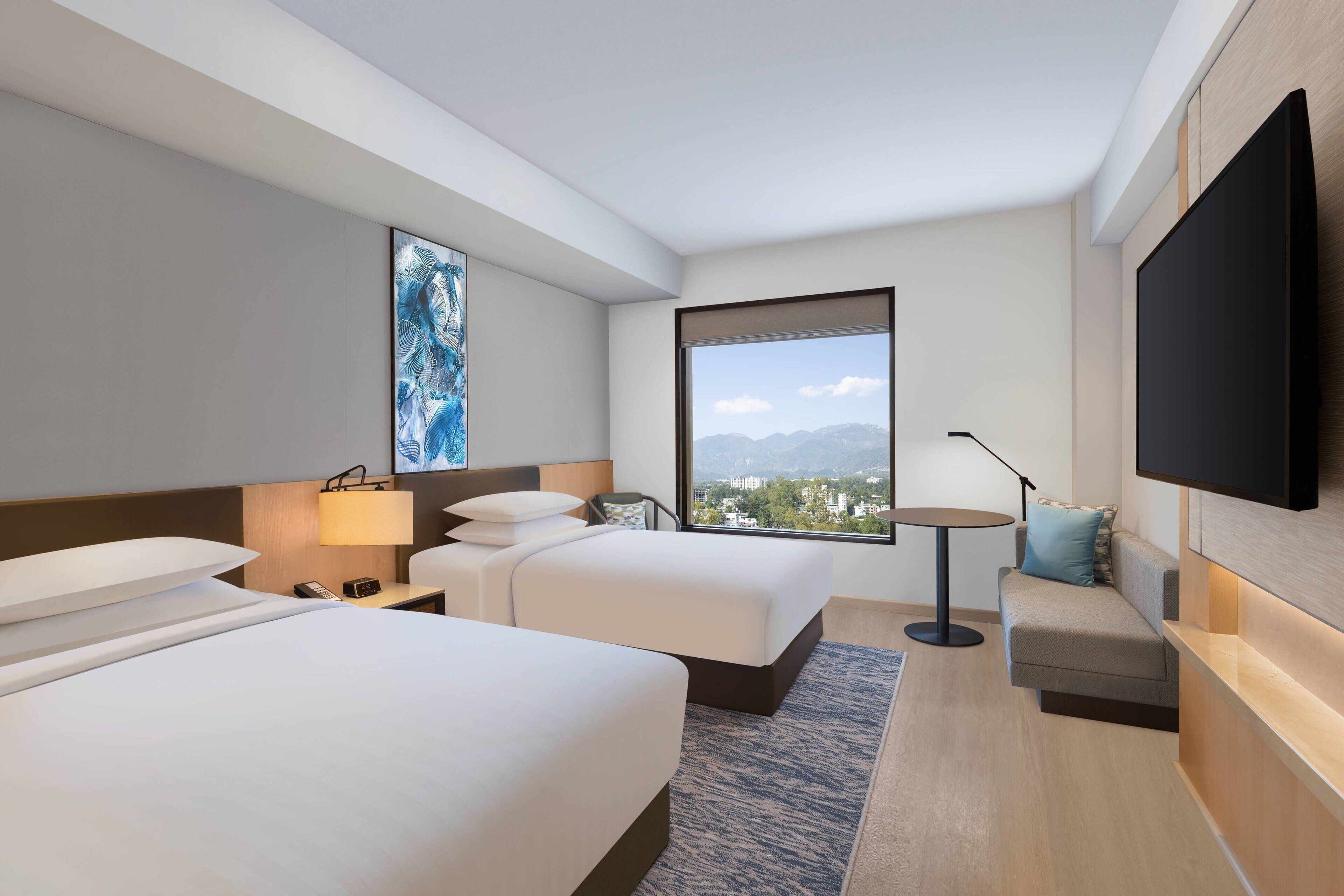 Une chambre d’hôtel avec deux lits, une télévision, un bureau et une fenêtre donnant sur la ville.