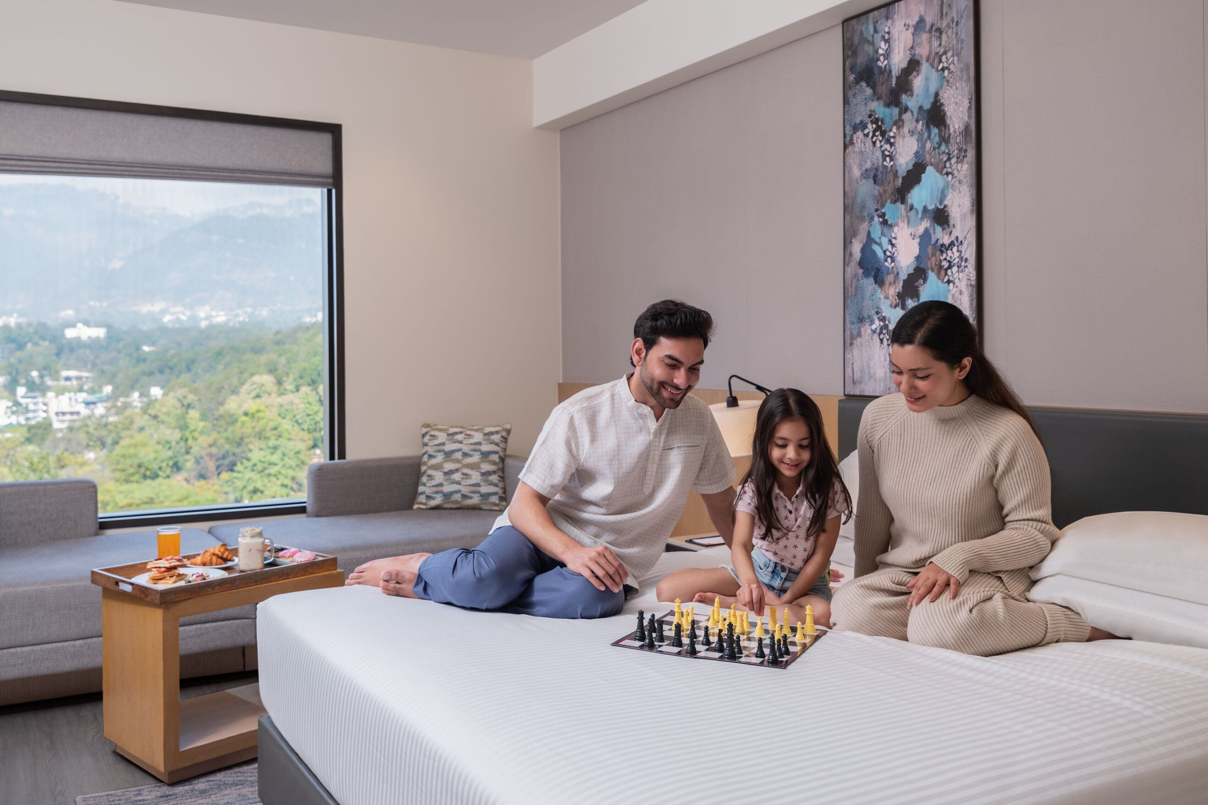 A hotel room with a bed, a coffee table with breakfast, and a chessboard.