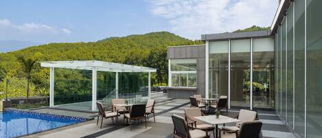 A modern outdoor patio with a pool, seating area, and a glass-enclosed structure.