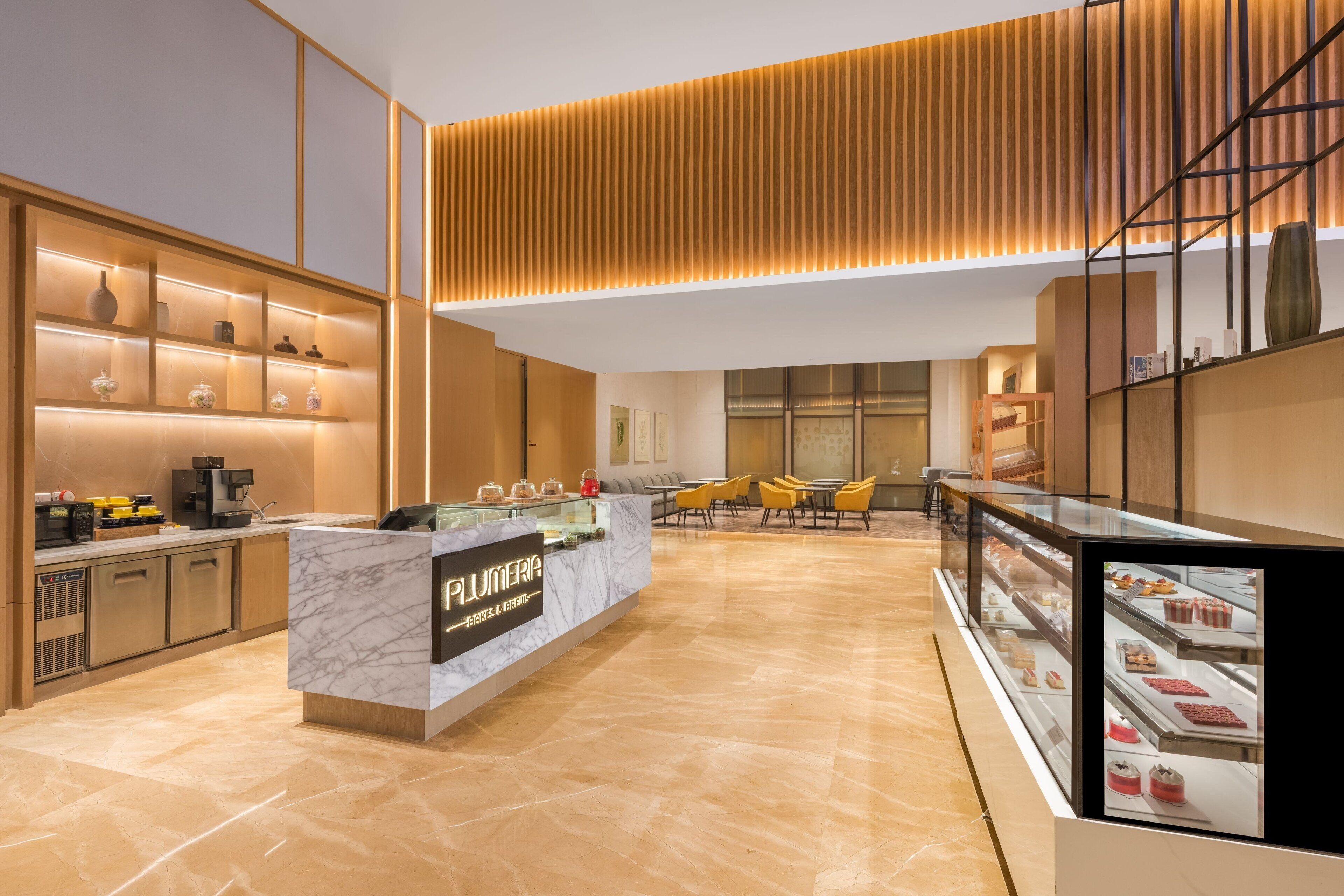 A modern hotel lobby with a marble reception desk, a coffee machine, and a seating area with yellow chairs.