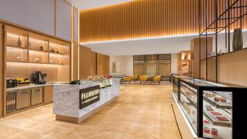 A modern hotel lobby with a marble reception desk, a coffee machine, and a seating area with yellow chairs.