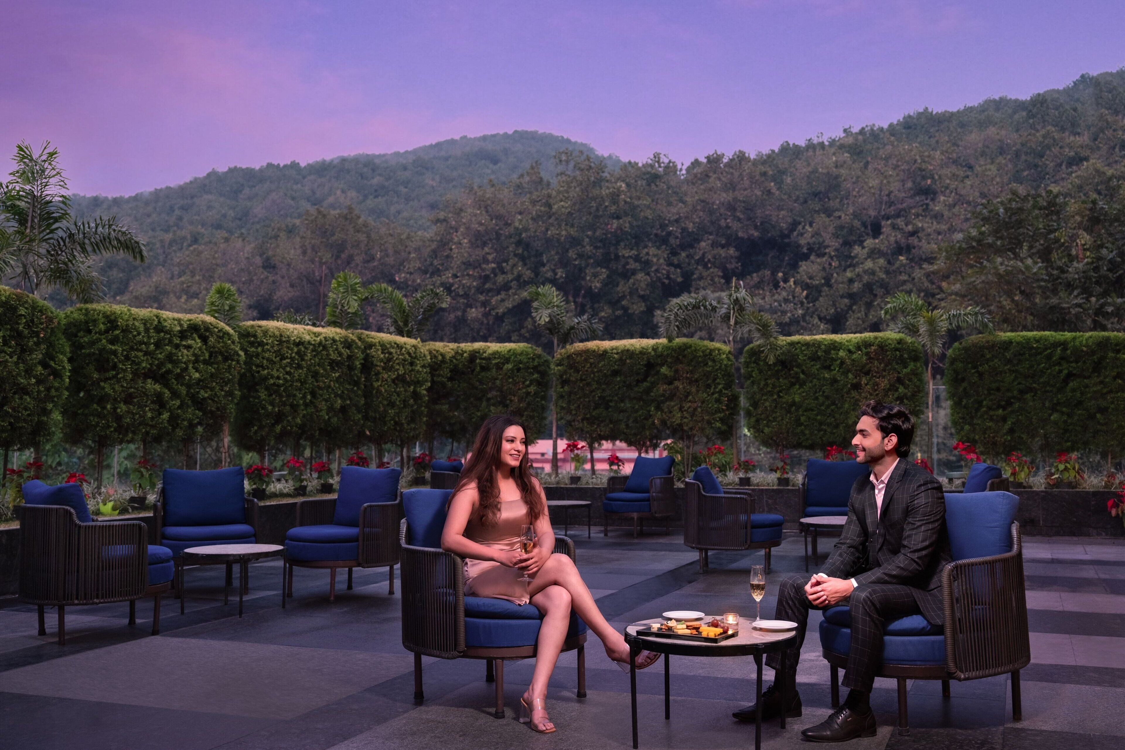 Two people seated at a table outdoors with a mountainous backdrop.