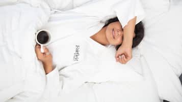 Una persona sdraiata su un letto con una tazza di caffè, indossa una veste bianca.