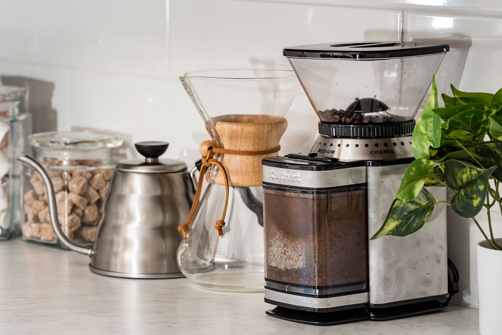 Une cuisine équipée d’une machine à café, d’un récipient en verre contenant des grains de café, d’une casserole en métal et d’une plante en pot.