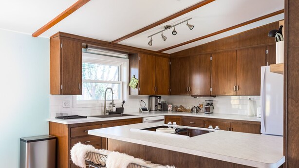 Eine moderne Küche mit Holzausstattung, einer großen Kochinsel mit Barhocker, einem Edelstahlkühlschrank und einem Fenster für natürliches Licht.