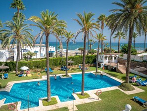 A pool area with clear blue water, surrounded by palm trees and lounge chairs. - Marina Real Paradise Views 5009 (Manilva)