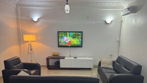 Un soggiorno con una televisione a schermo piatto, due divani neri, un mobile bianco per l'intrattenimento, una lampada da terra e un condizionatore d'aria.