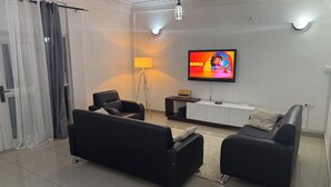 Un soggiorno moderno con una TV a schermo piatto, due divani neri, una lampada da terra e un tavolino con il simbolo WiFi.