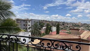 Un balcone con ringhiere in ferro battuto affaccia su una città con edifici, palme e cielo sereno.