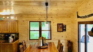 Un interior de madera con una mesa de comedor, sillas y una zona de cocina con armarios y un ventanal.