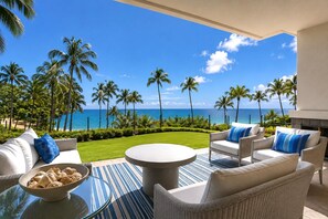 Eine Terrasse mit Gartenmöbeln, einer Schale Kekse und Blick auf den Ozean und Palmen.