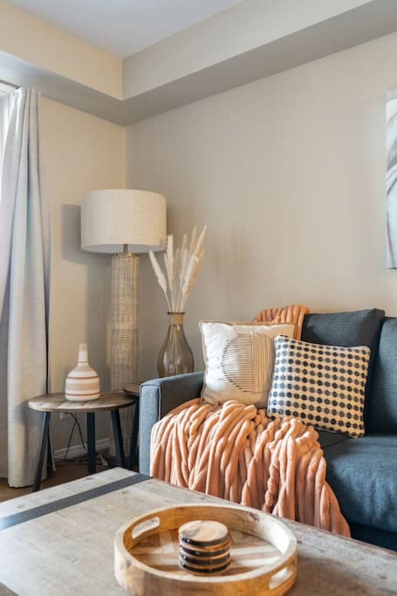 Een moderne woonkamer met een grijze bank, een gebloemd plaid en een lamp op een bijzettafeltje.