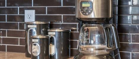 Eine Kaffeemaschine mit Digitalanzeige, ein Teebehälter und zwei Zuckerdosen auf einer Küchenarbeitsplatte.