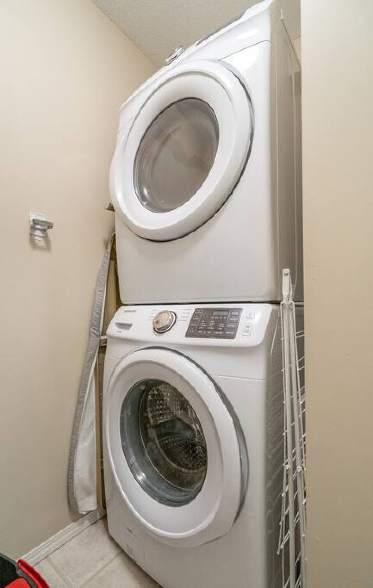 A stacked washer and dryer unit in a laundry room with a tiled floor and a towel rack.