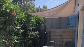 A patio area with a table and chairs, surrounded by greenery and a wooden fence.