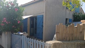 A house with a blue door, a white fence, and a potted plant with pink flowers.