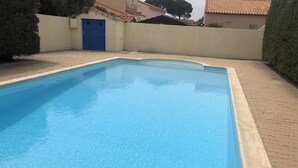 A rectangular swimming pool with a tiled edge, surrounded by a paved walkway and a low wall.