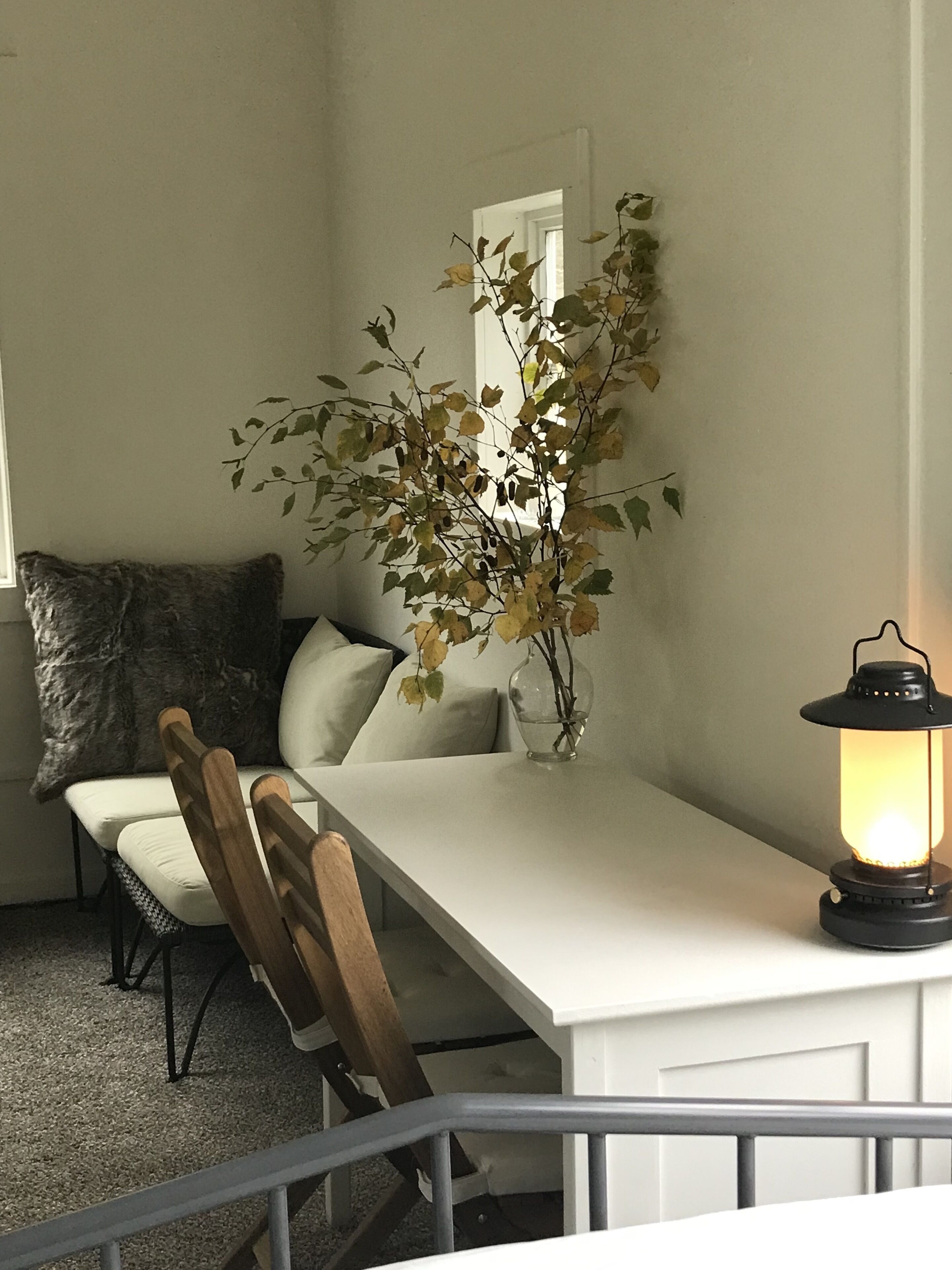 A dining area with a white table, wooden chairs, a small potted plant, and a lit lantern.