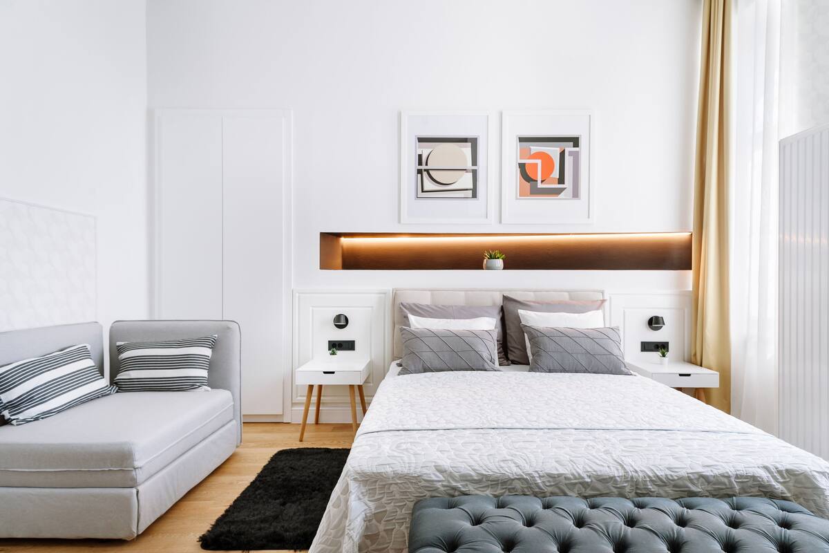 A modern bedroom with a bed, a sofa, and a nightstand with a lamp.