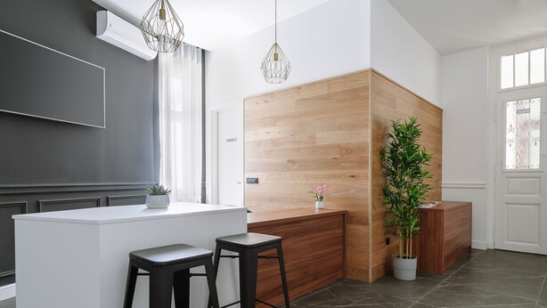 A modern kitchen with a white countertop, two black stools, a wooden accent wall, and a potted plant.