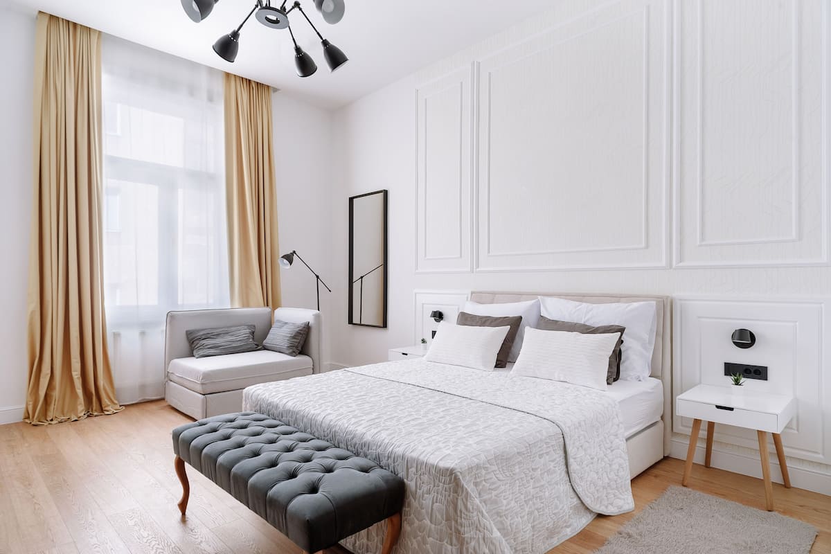 A modern bedroom with a large bed, a bedside table, a chair, and a window with curtains.