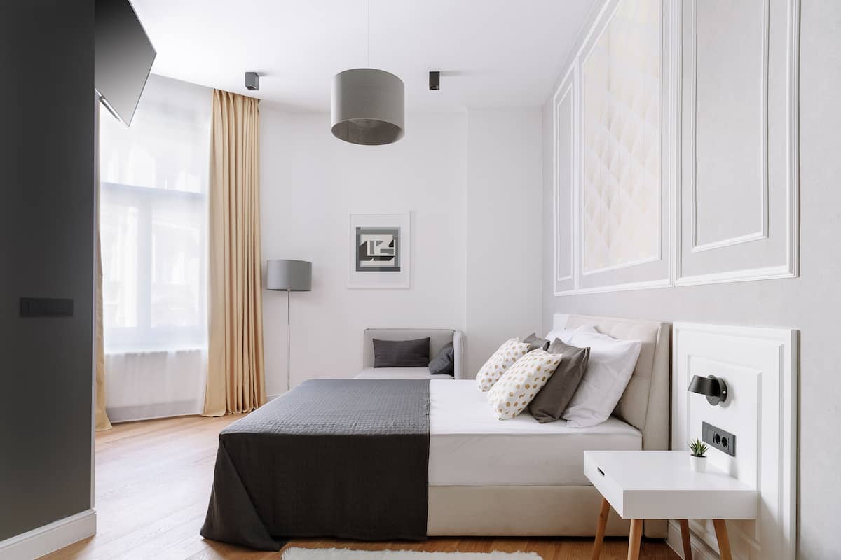 A modern bedroom with a bed, bedside table, and a large window with curtains.