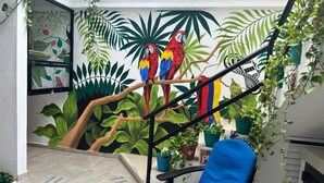 A room with a mural of parrots on a tree branch, a blue chair, and potted plants.