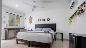 A bedroom with a bed, a desk, a chair, a ceiling fan, an air conditioner, and a refrigerator.