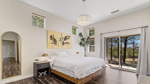 A bedroom with a large bed, a nightstand, a mirror, a chandelier, and a view of the outdoors through a sliding glass door. - Upscale, Nature Views, Family Retreat for a great Mountain Getaway (Flagstaff)