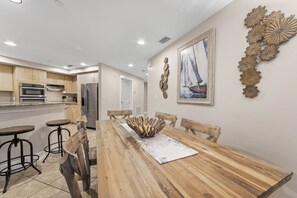 Una cocina moderna con armarios de madera, electrodomésticos de acero inoxidable y un comedor con mesa de madera y taburetes de bar.