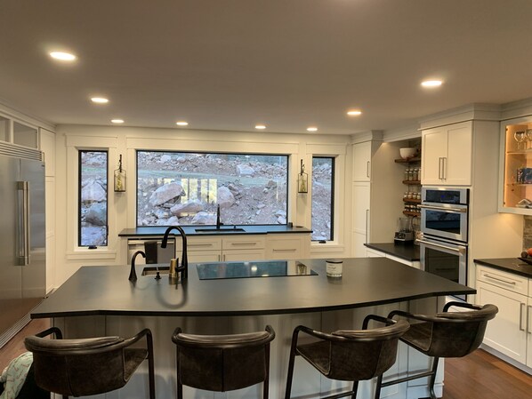 A modern kitchen with a large island, bar stools, and a view of a rocky landscape through large windows.