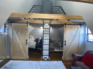 A loft bedroom with a wooden ceiling, a loft bed, and a ladder leading to the bed.