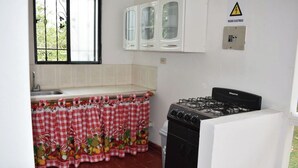 Cozinha com fogão a gás, pia e janela com cortinas decorativas.