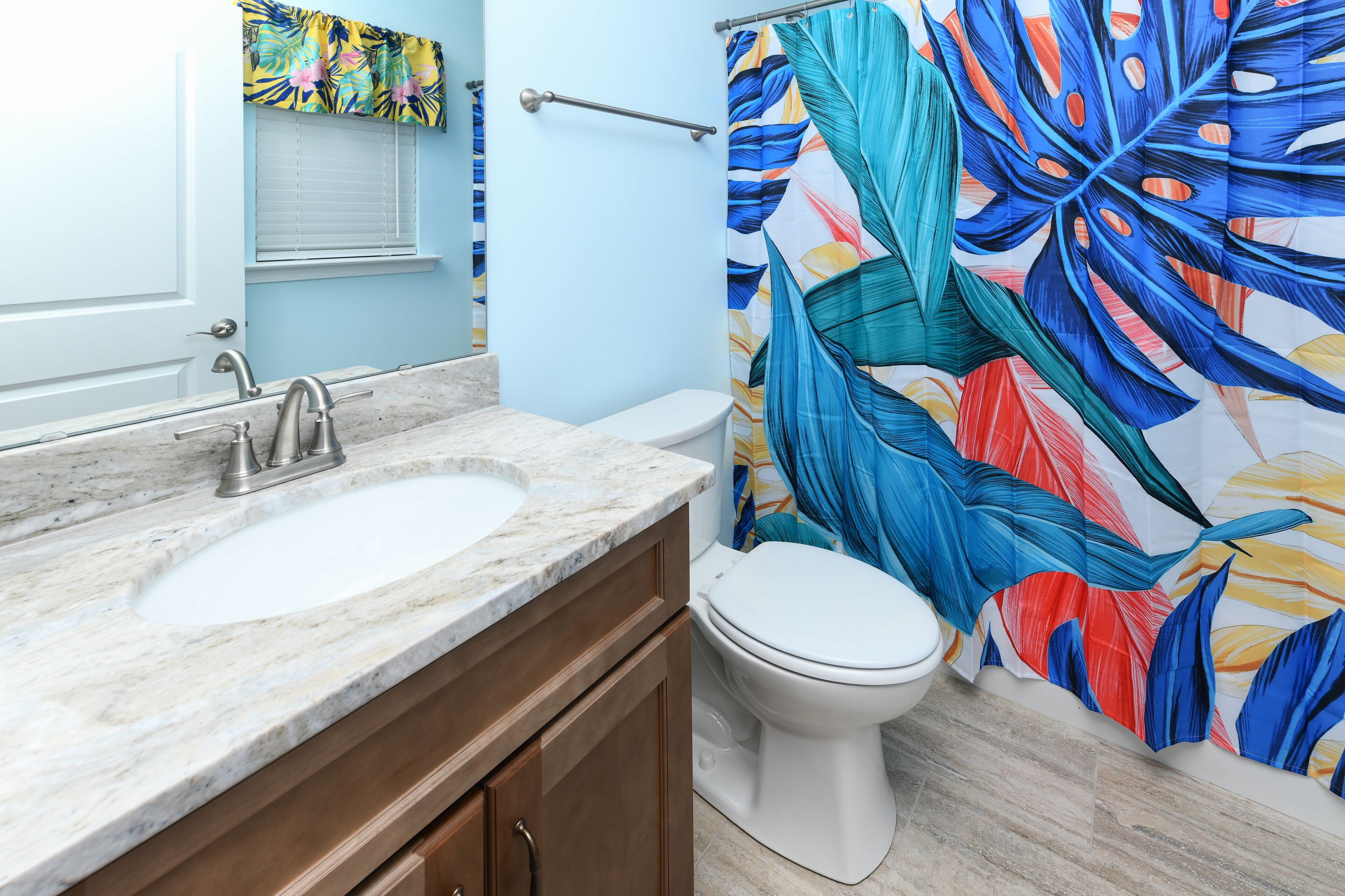 A bathroom with a marble sink, wooden cabinets, a white toilet, and a shower curtain with a tropical leaf pattern.