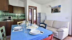 Un comedor con una mesa azul dispuesta para cuatro, un sofá beige y una cocina con armarios de madera y salpicadero de azulejos.
