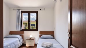 Un dormitorio con dos camas, una ventana que da a un edificio, una mesita de noche con lámpara y una puerta.
