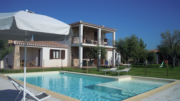 Un edificio de dos pisos con piscina, mobiliario exterior y una sombrilla blanca.