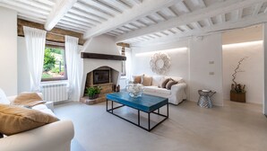 A living room with a fireplace, white sofas, a coffee table, and a view of greenery outside. - Villa Casanostra 12, Emma Villas (San Ginesio)