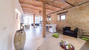 A spacious interior with exposed brick walls, a large stone vase, and a dining area with a table set for two. - Villa Casanostra 12, Emma Villas (San Ginesio)