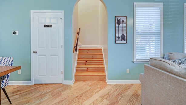 A hallway with a wooden staircase, a door labeled "PRIVATE," a framed picture, and a window with blinds.