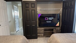 A hotel room with two beds, a TV on a wooden stand, and a door leading to another room.
