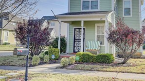 A two-story house with a green exterior, a front porch with a bench, and a mailbox.