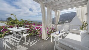 Un espace extérieur aménagé avec des sièges blancs, comprenant une table et des chaises, entouré de rideaux blancs et offrant une vue sur le paysage.