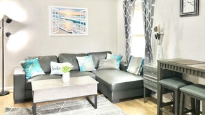 A modern living room with a sectional sofa, a coffee table, and a dining area with a small table and stools. - Brilliant Bungalow (Dayton)