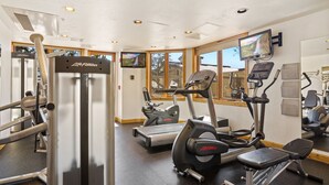 Een sportschool met cardioapparatuur, krachttrainingsapparatuur en een televisiescherm.