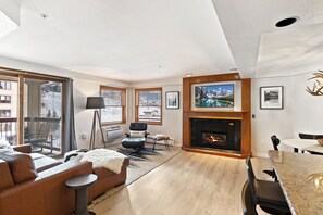 Una sala de estar moderna con chimenea, un sofá, una mesa de comedor y ventanas amplias.